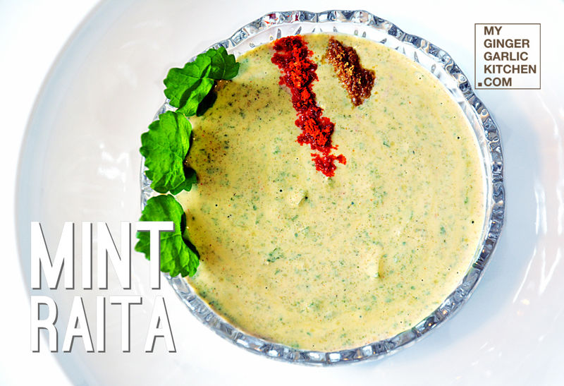 a bowl of mint raita with a sprinkle of spices and fresh mint leaves on top