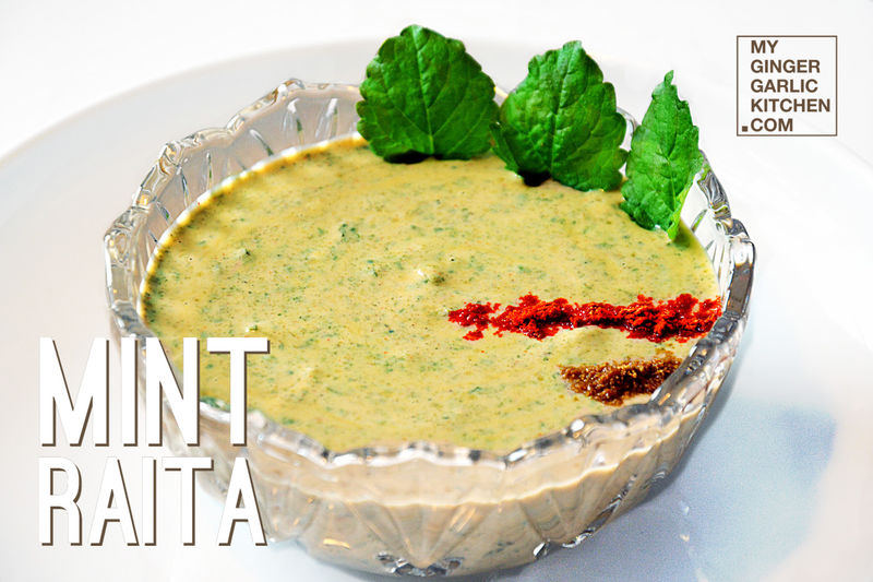 a bowl of mint raita with a sprinkle of spices and fresh mint leaves on top on a table