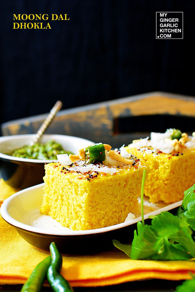 a plate of moong dal dhokla topped with coconut and green chilies