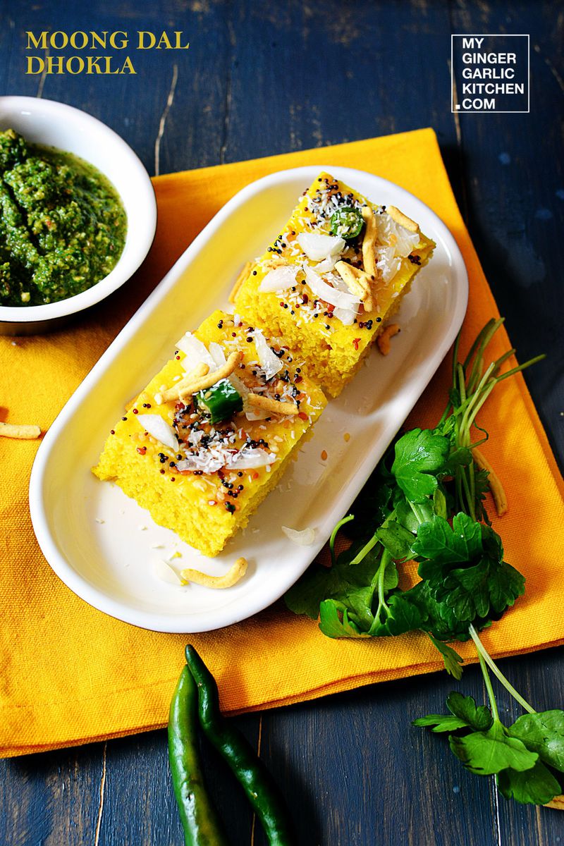 a plate of two moong dal dhokla with a side of green coriander chutney