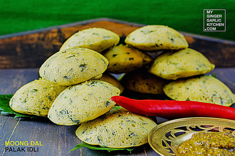a plate of moong dal palak idli with a chili and a bowl of dipping sauce