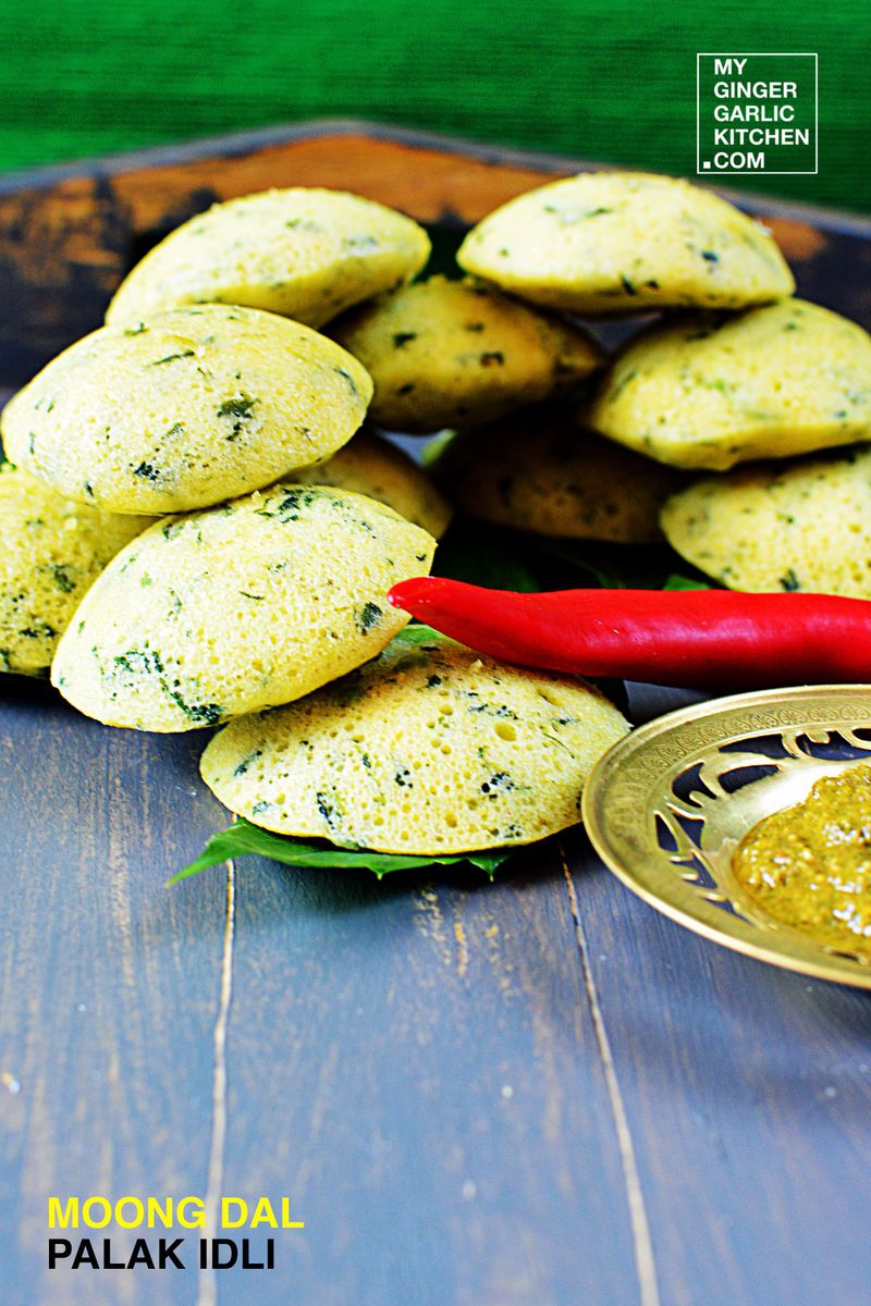 a tray of moong dal palak idli with a chili and a bowl of dipping sauce