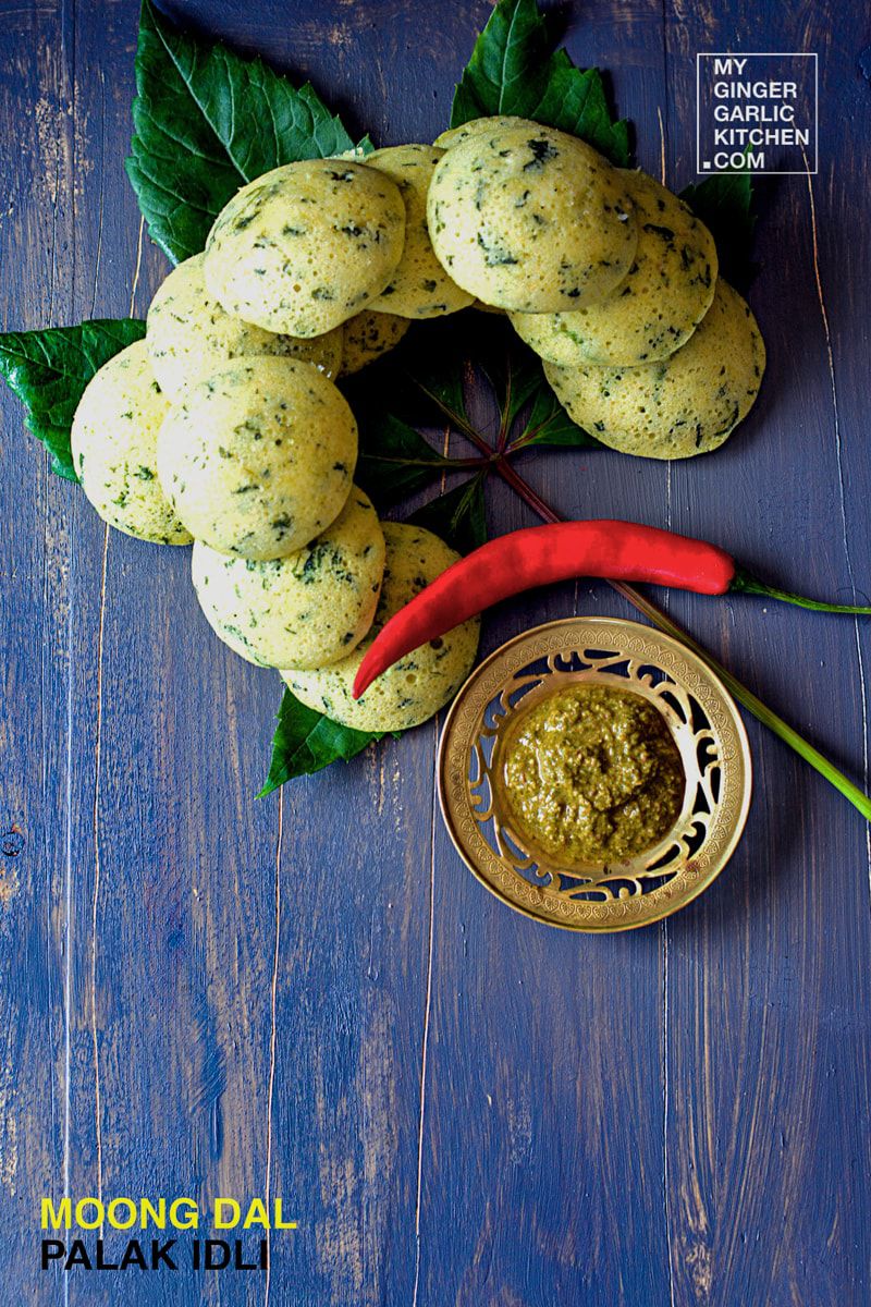 a plate of moong dal palak idli with a chili and a bowl of green sauce