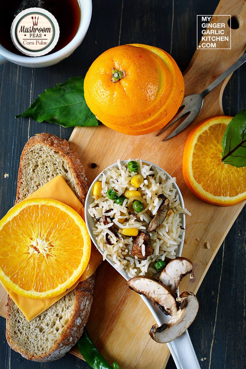 a wooden cutting board with a bowl of mushroom peas corn pulao and oranges