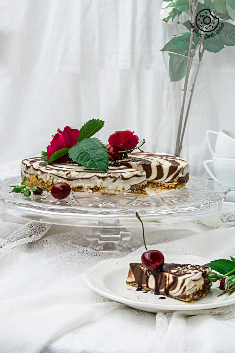 a no bake zebra cheesecake on a cake stand with a slice of cake in a plate