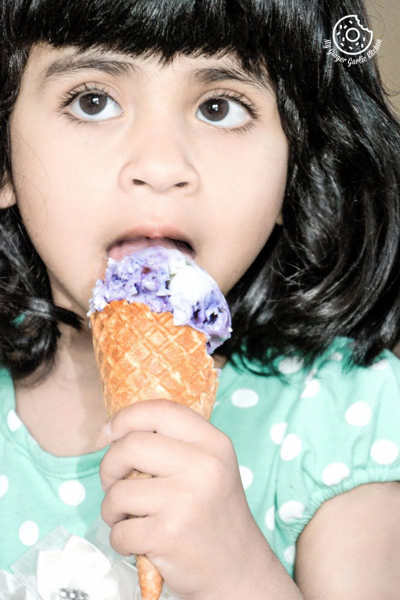a little girl eating a vegan coconut blueberry ice cream cone with purple flowers