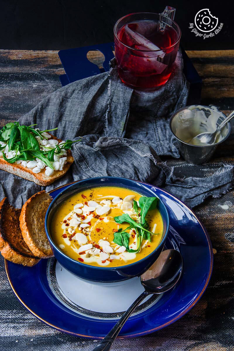 a bowl of creamy sweet potato carrot soup with bread and a spoon on a plate