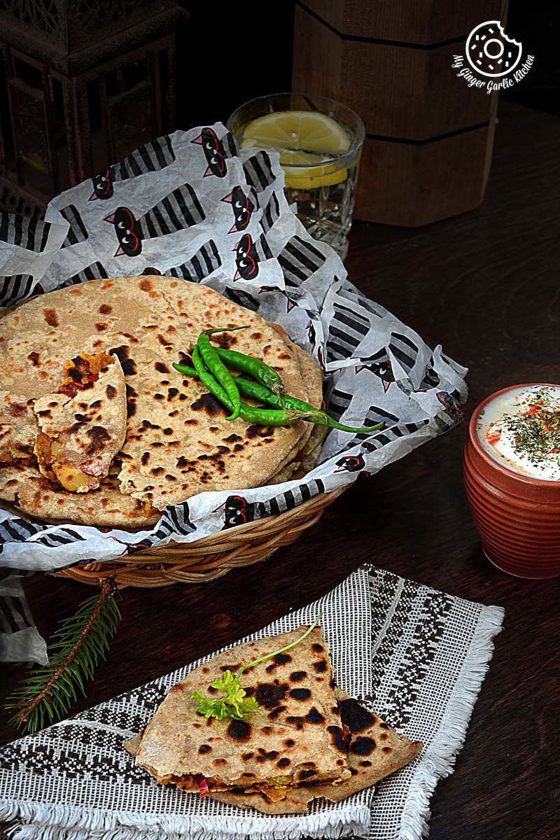 a basket of pepper onion potato paratha with green chilies on a table with a glass of lemon water