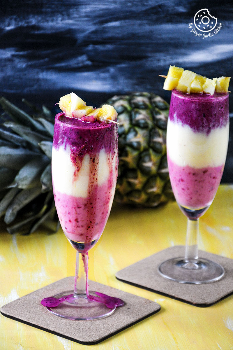 two glasses of pineapple blueberry raspberry breakfast layered smoothie on a table