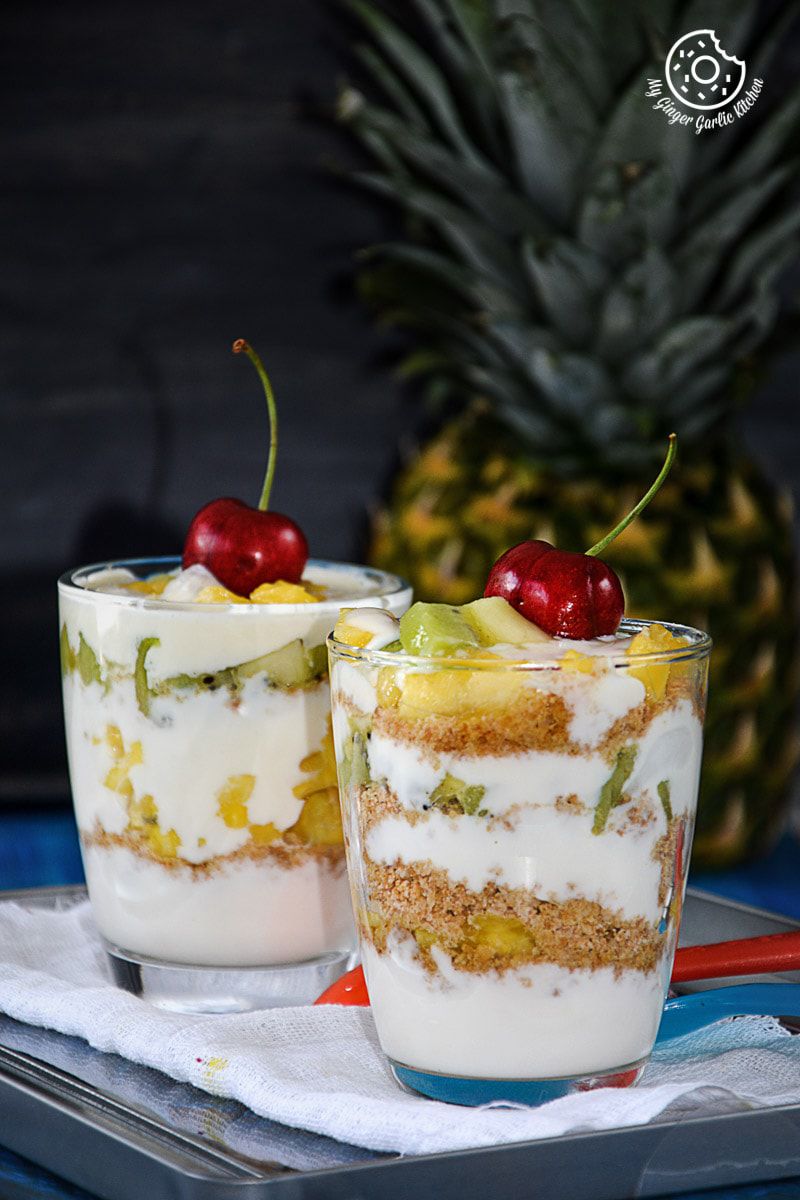 two pineapple kiwi yogurt parfaits in small cups with fruit on top