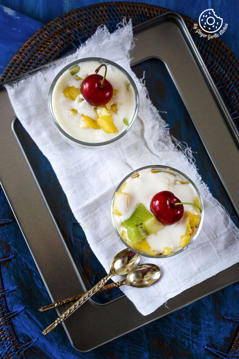 two small pineapple kiwi yogurt parfaits with cherries on a tray