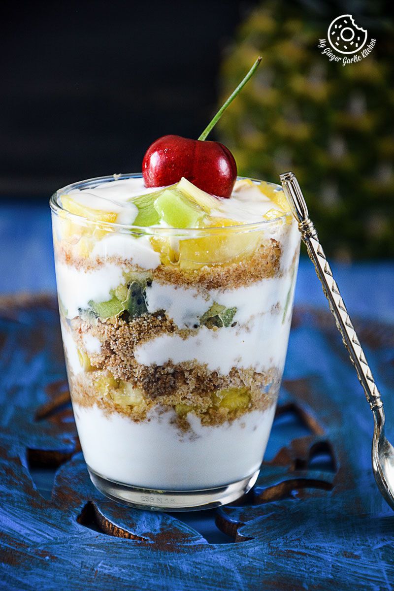pineapple kiwi yogurt parfait in a glass with a spoon and a cherry on top