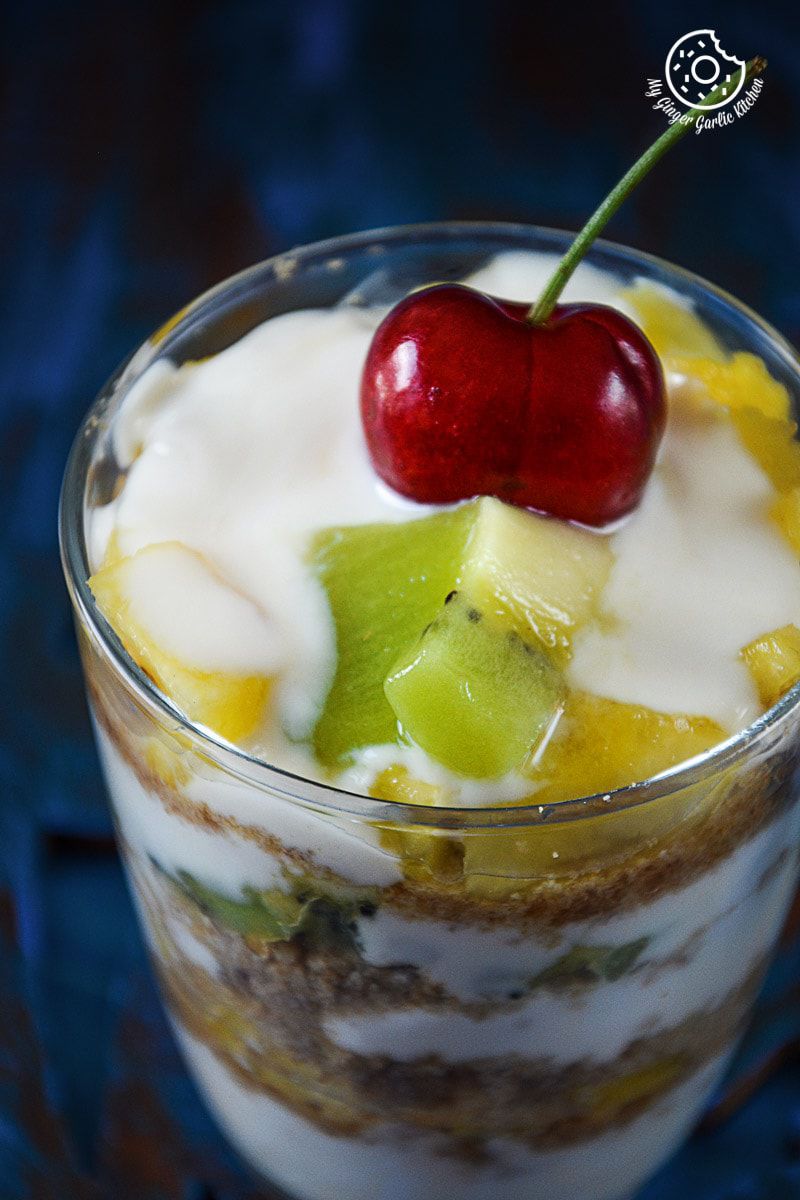 a glass of pineapple kiwi yogurt parfait with a cherry on top