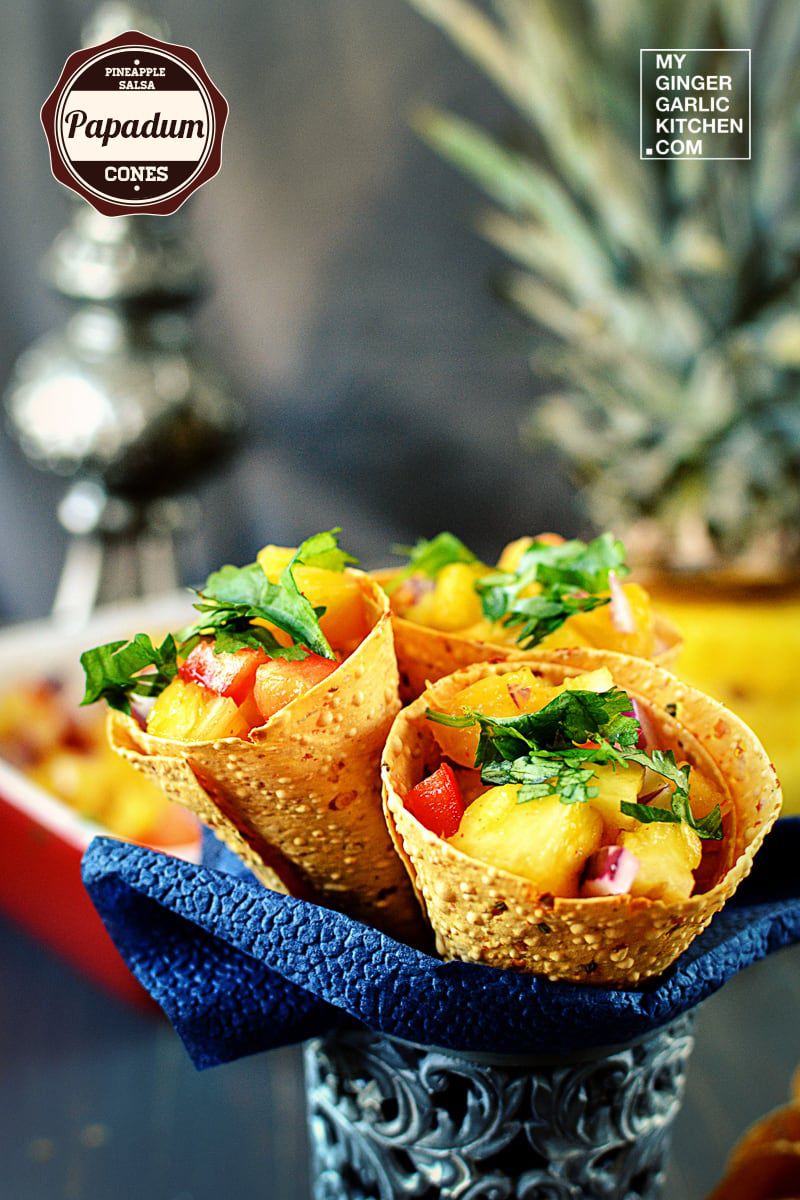three pineapple salsa papadum cones on a blue napkin with pineapples in the background