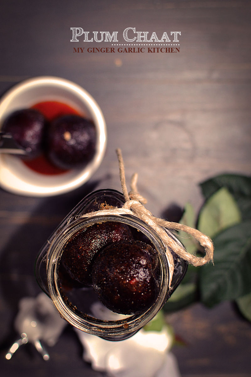a jar of plum jam with a spoon and a bowl of plums