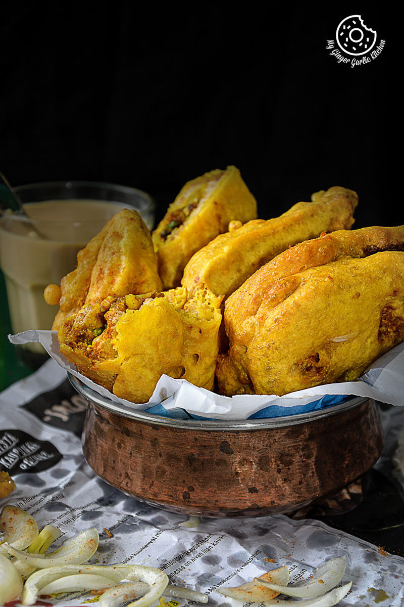 a copper bowl of fried potato stuffed bread pakora on a table with a glass of coffee