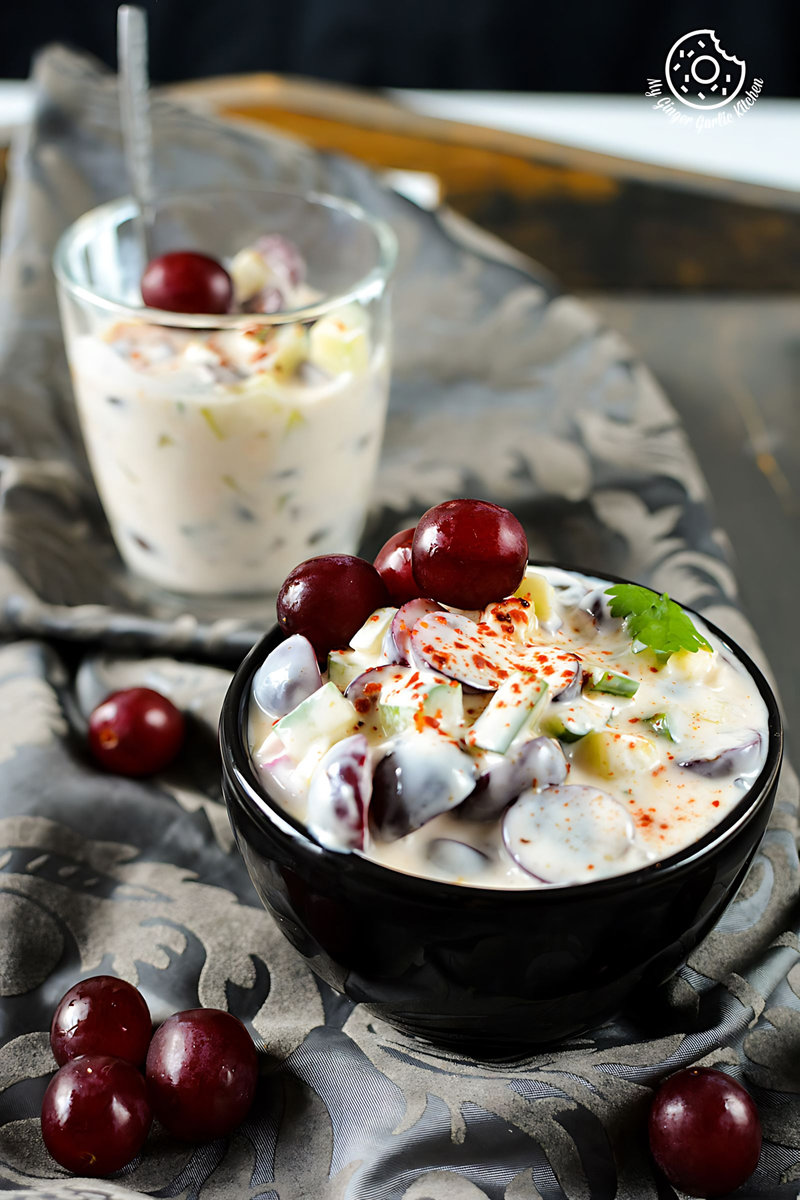 a bowl of red grapes onion cucumber raita with more grapes on the side