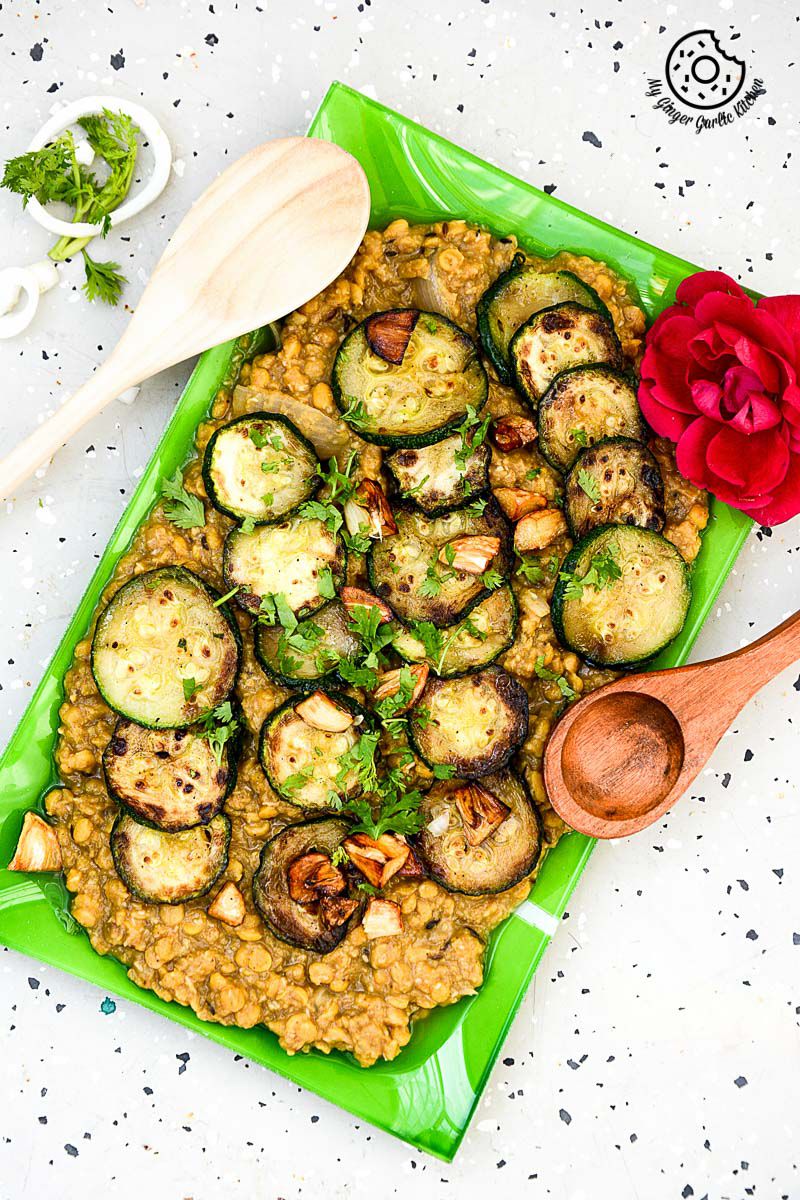 a green plate with a serving of roasted zucchini garlic with spiced chana dal on it