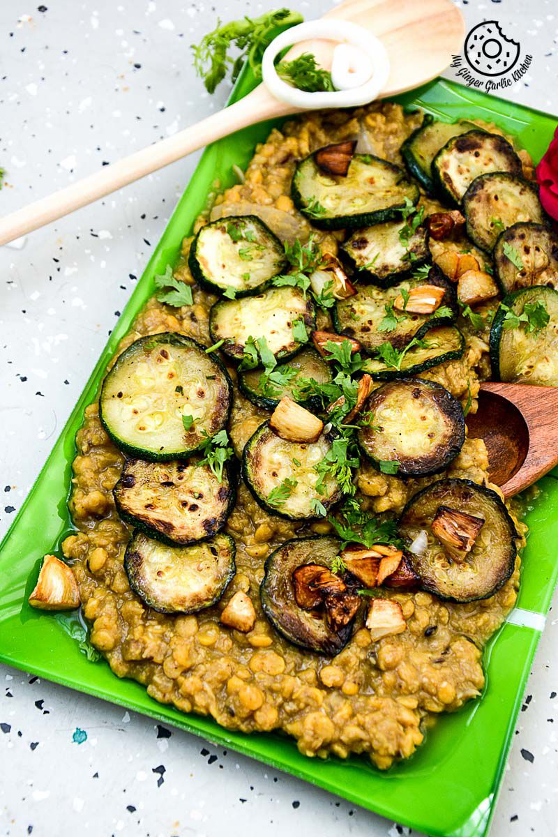 a green plate with a green plate of roasted zucchini garlic with chana dal on it
