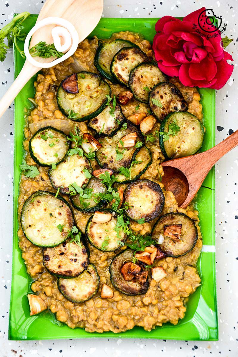 a green plate with a green plate of roasted zucchini garlic with chana dal and red rose with two wooden spoons