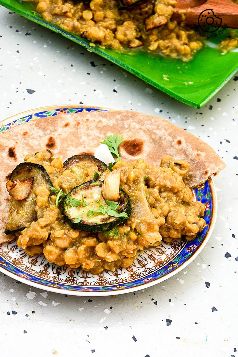 a plate of roasted zucchini garlic with spiced chana dal with paratha that is on a table