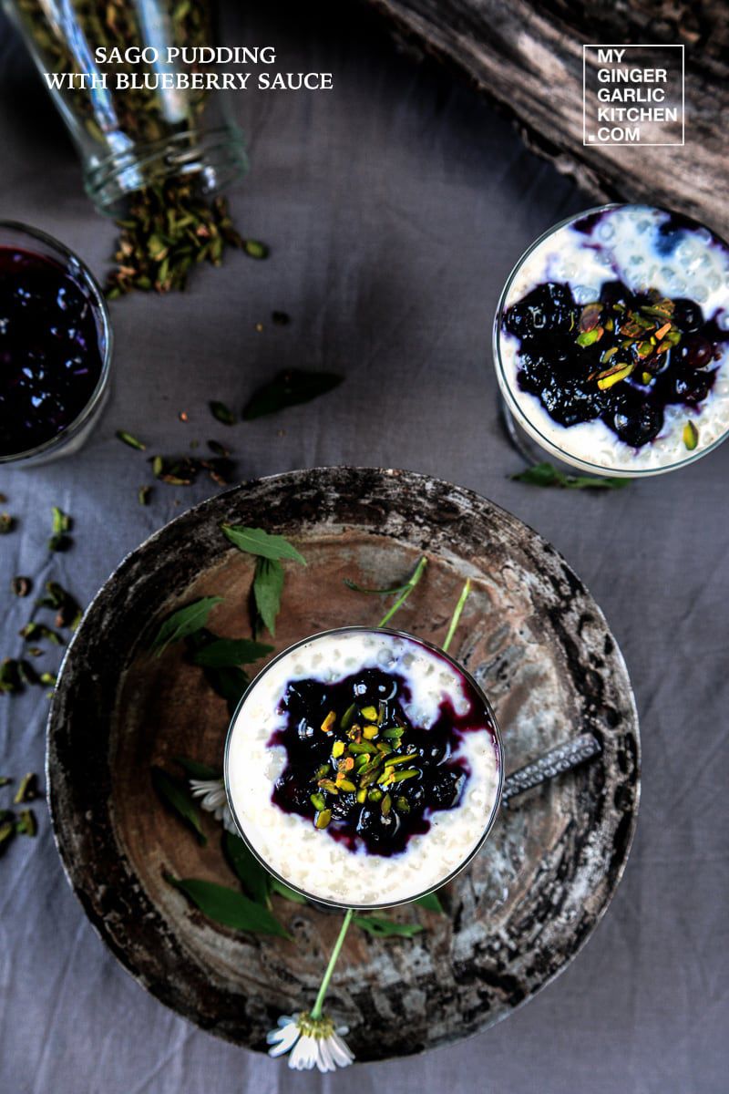 a sago pudding with blueberry sauce and pistas in a glass with one more glass on the side