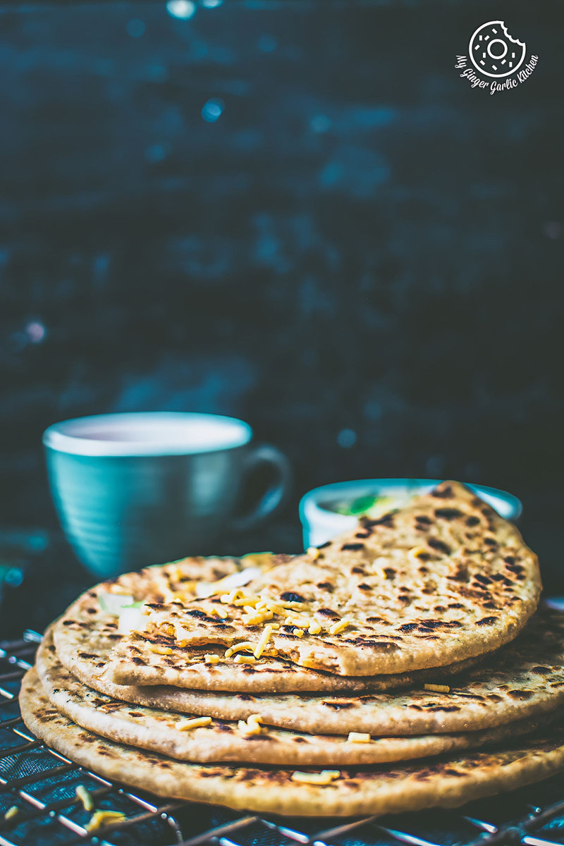 three sev stuffed paratha aka bhujiya parathas stacked on a cooling rack with a cup of coffee