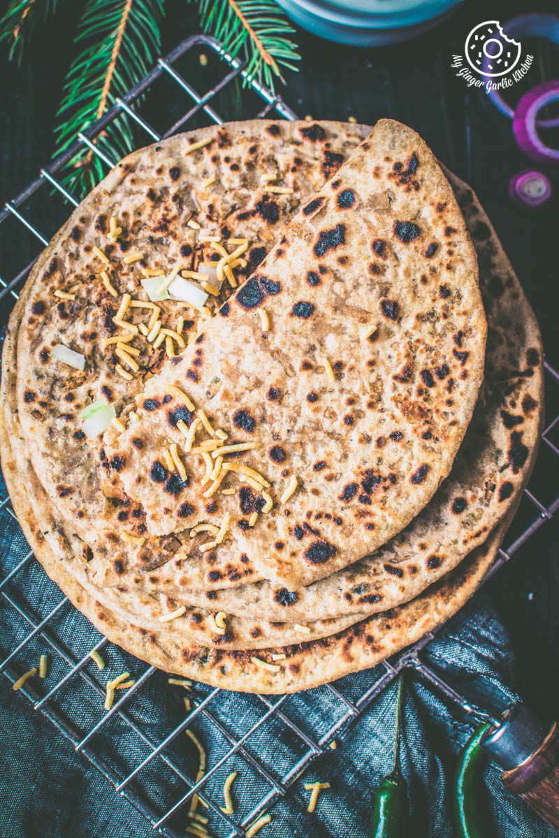 a stack of bhujiya paratha on a cooling rack with some namkeen on top