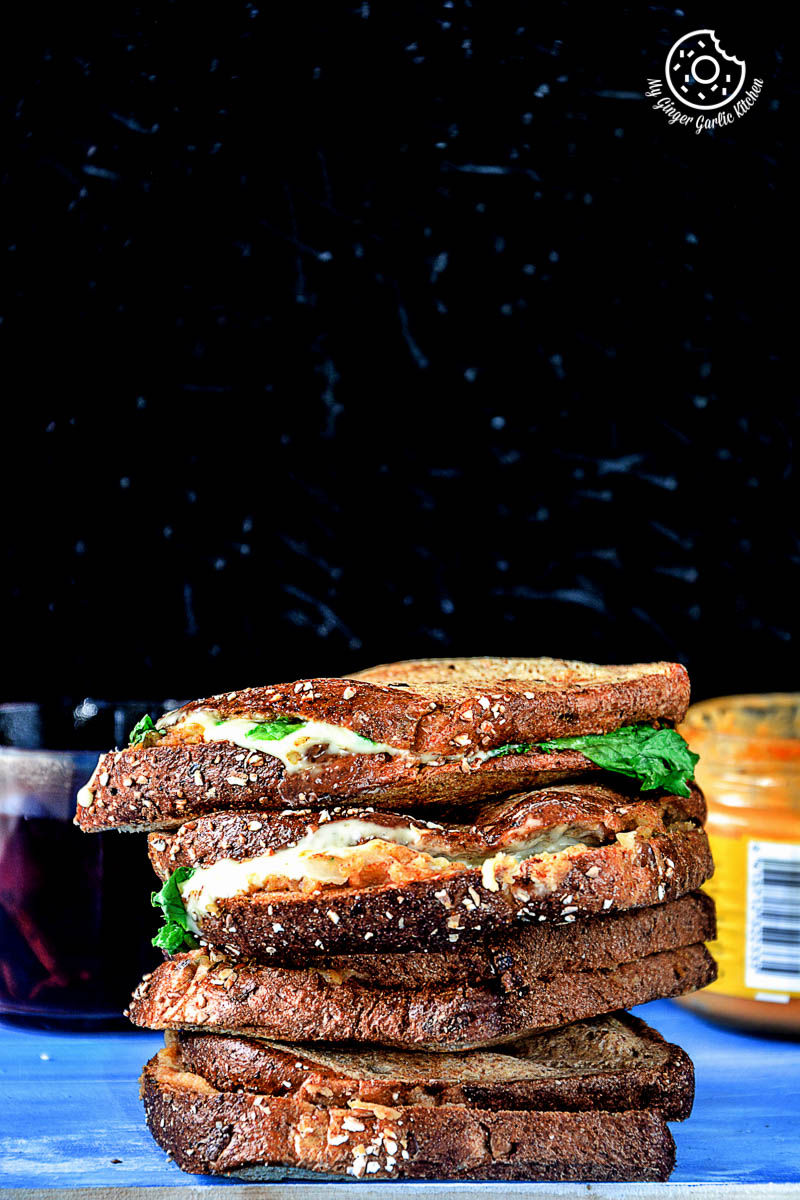 a stack of spiced potato cheese sandwiches on a tray with a jar of mustard