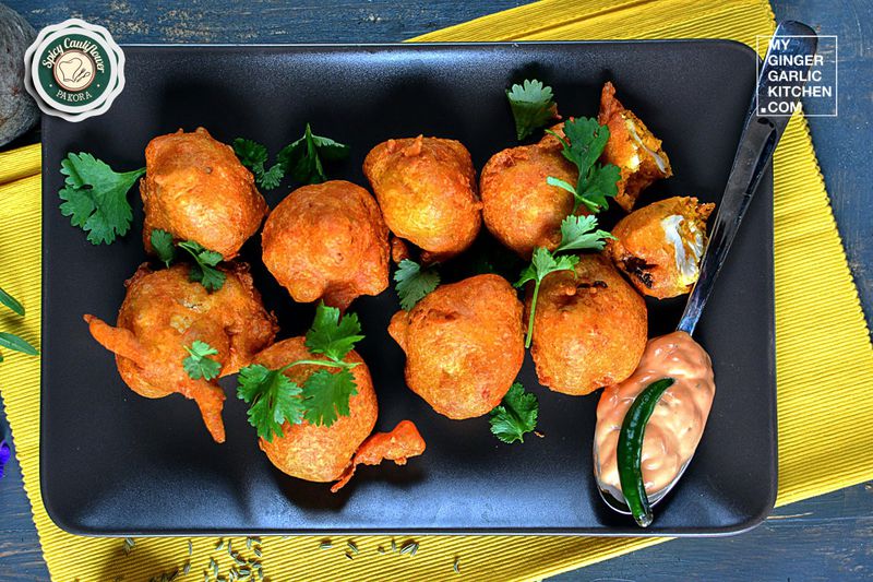 a plate of cauliflower pakora with cilantro, sauce and a spoon on a table