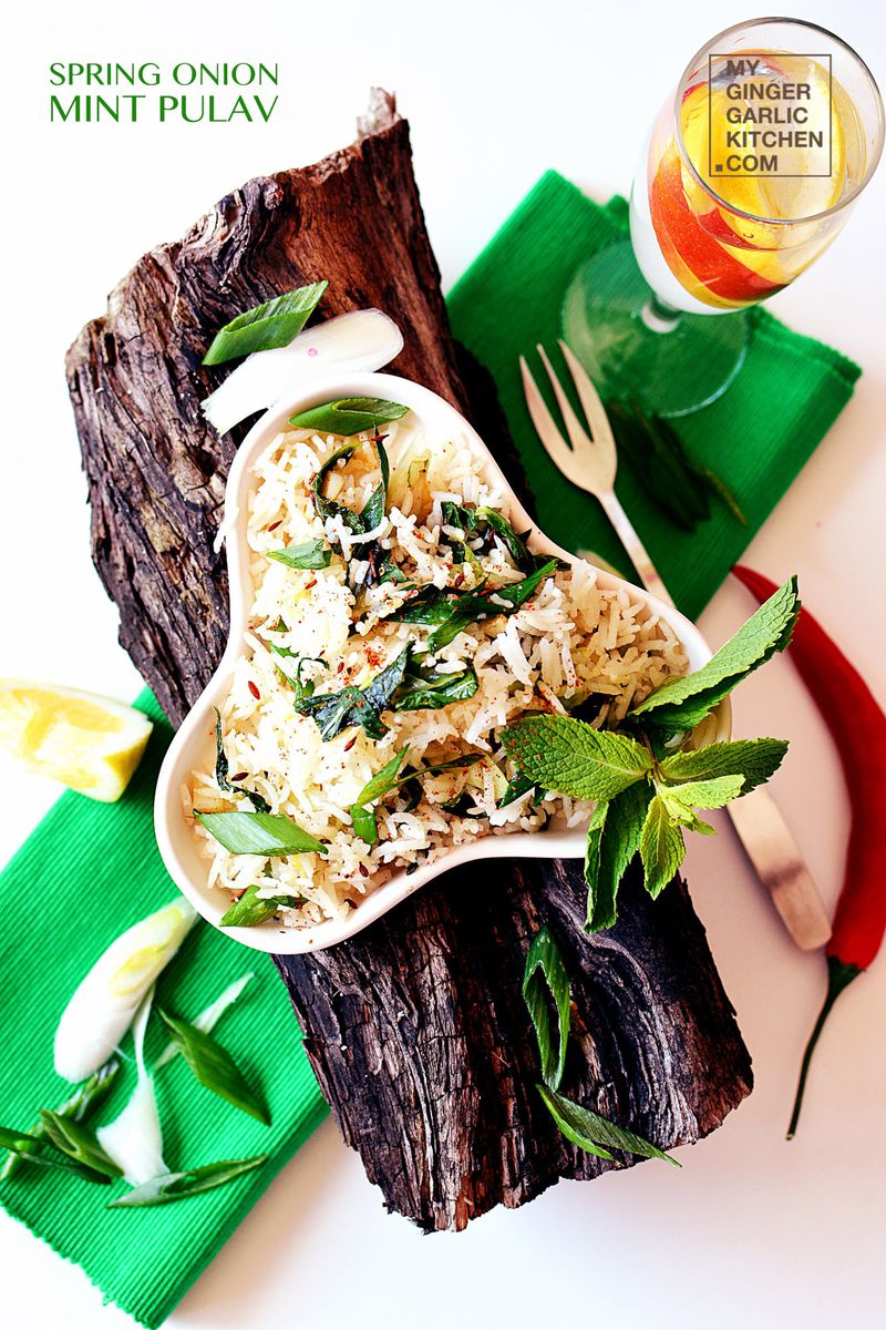 a plate of spring onion mint pulao on a wooden table with a glass of water