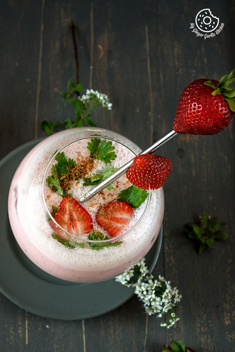 a glass filled with strawberry masala chaas with strawberries and mint leaves in it