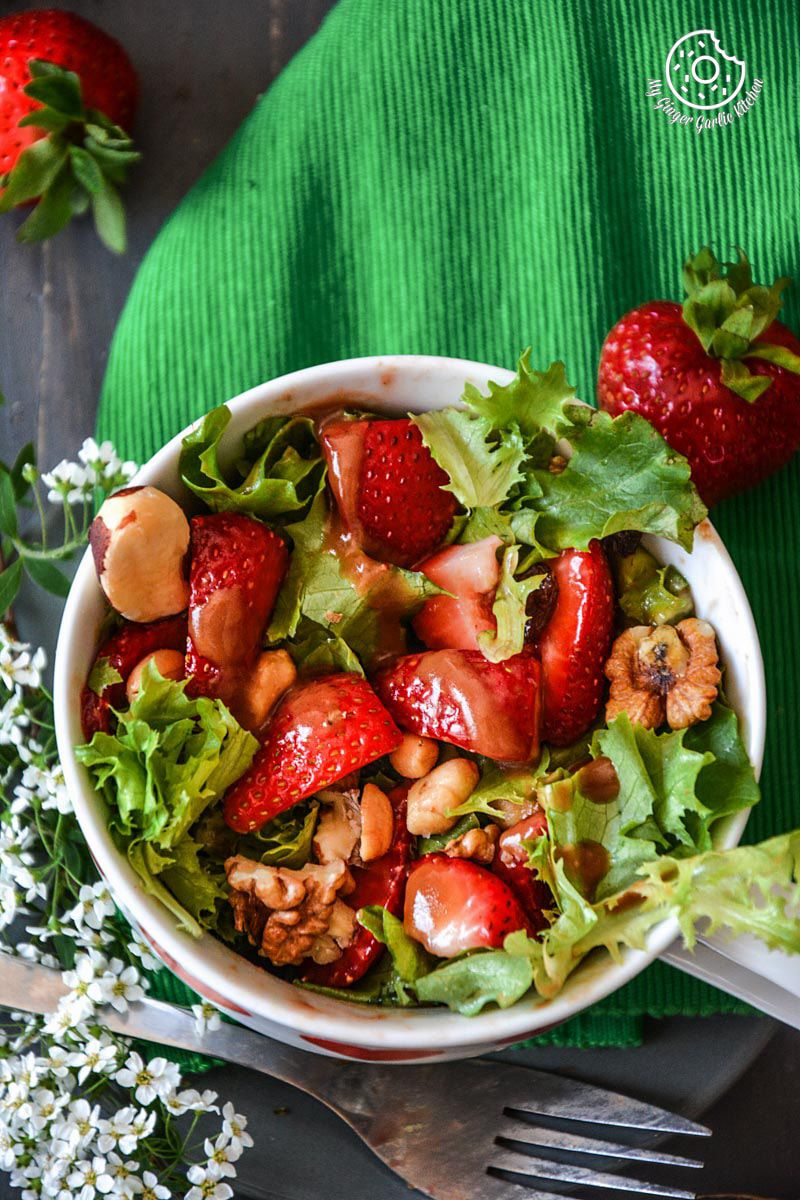 a bowl of summer berry salad with salted with peanuts and walnuts in it on a green napkin