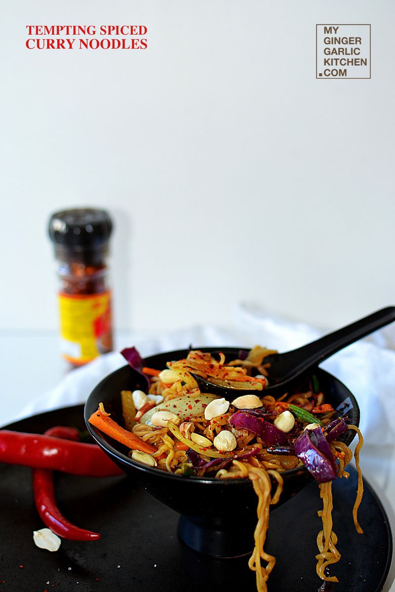 a bowl of spiced curry noodles with a spoon and a pepper