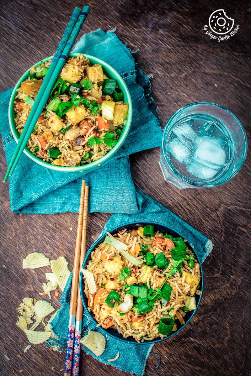 two bowls of thai pineapple fried rice vegan with chopsticks and a glass of water
