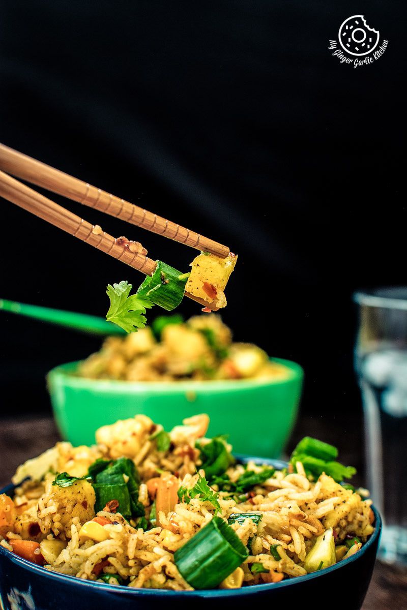 chopsticks lifting up a bowl of thai pineapple fried rice vegan from a bowl