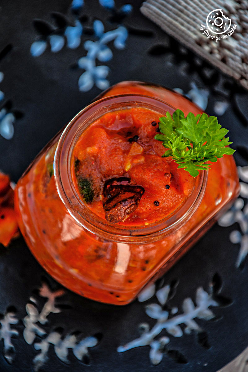 a jar of tomato mustard garlic chutney topped with parsley sitting on a plate