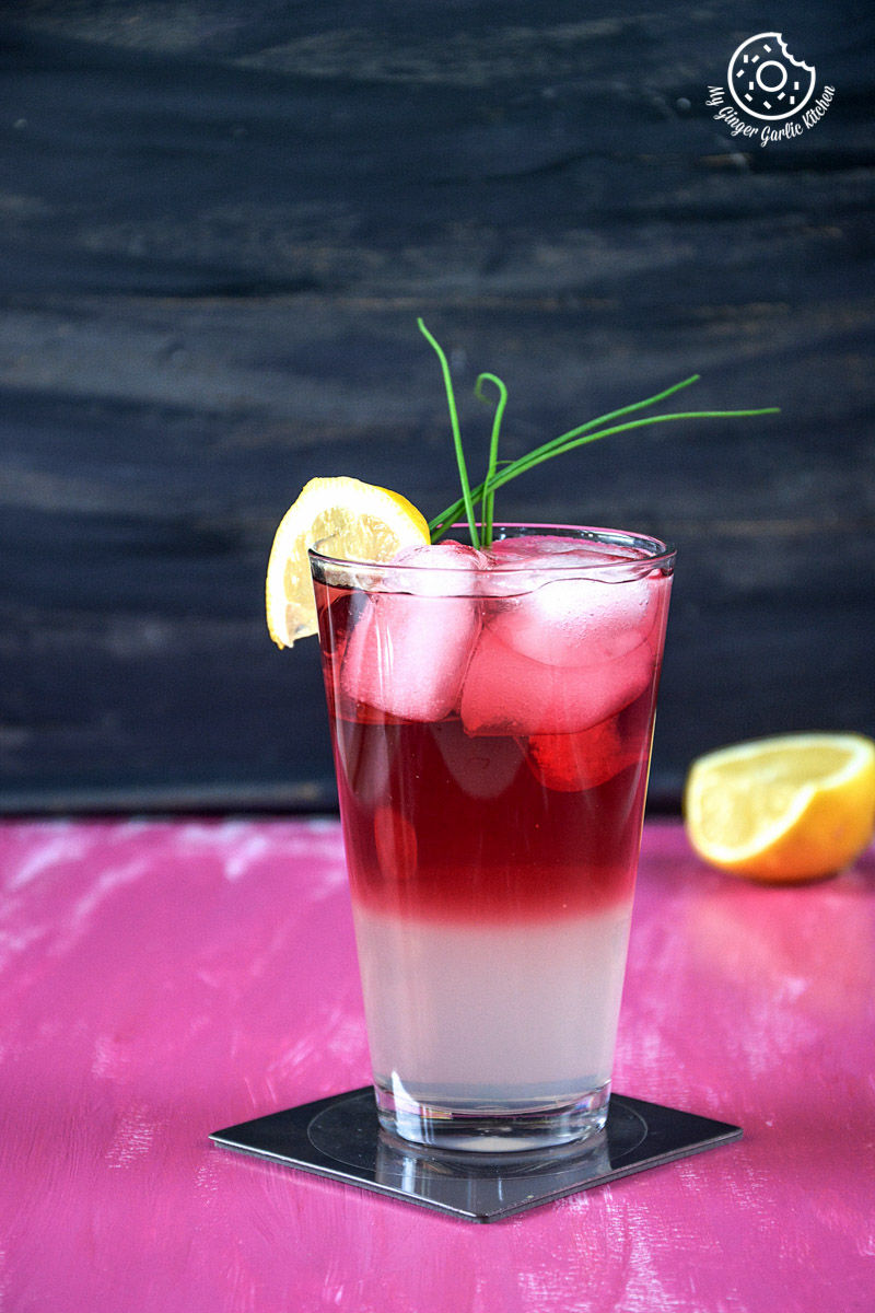 a glass of watermelon lemonade with ice and lemon wedges