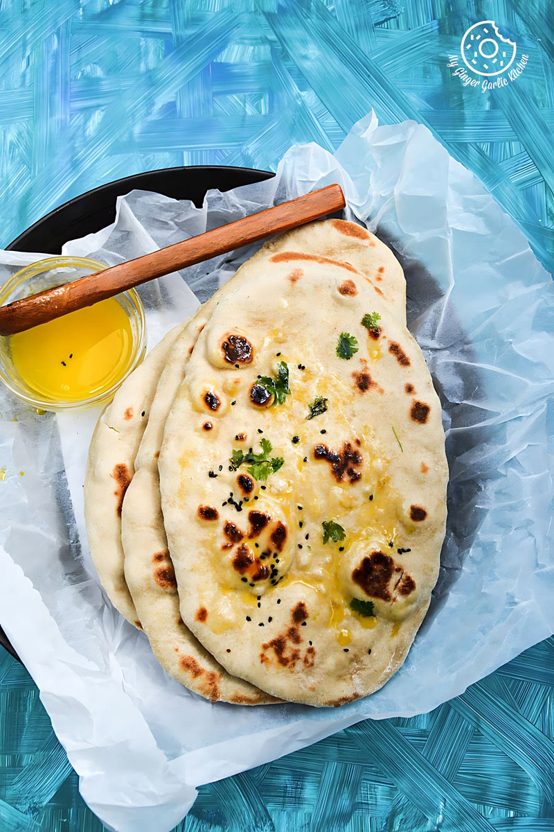 there is a plate of  whole wheat naan with a wooden spoon and a bowl of ghee