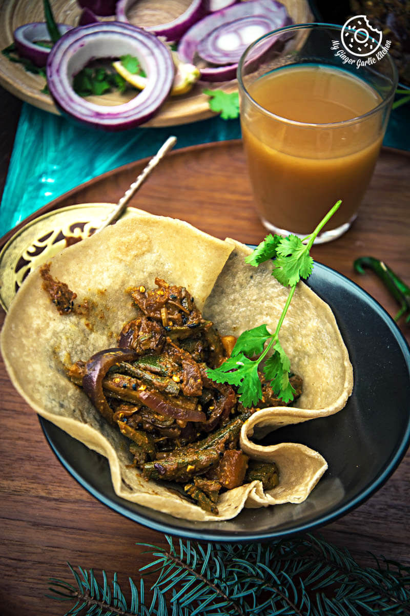a plate of pad wali roti topped with achaari dahi bhindi and a glass of orange juice