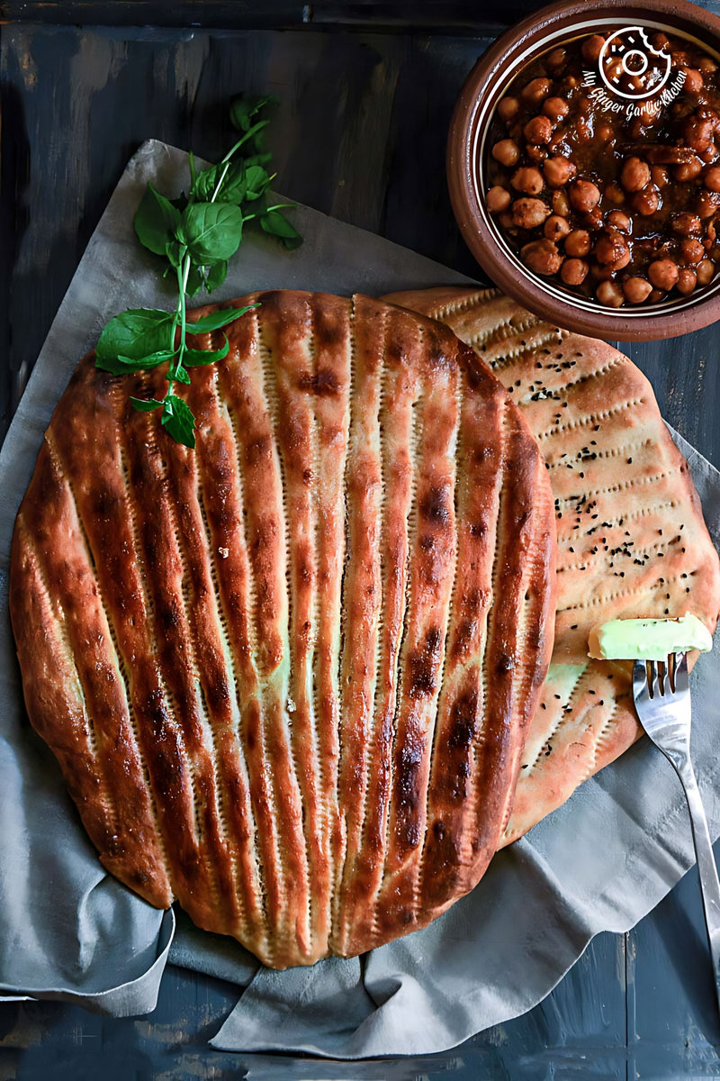 a plate of afghan naan bread with a mint leaf and a bowl of chole masala on a table