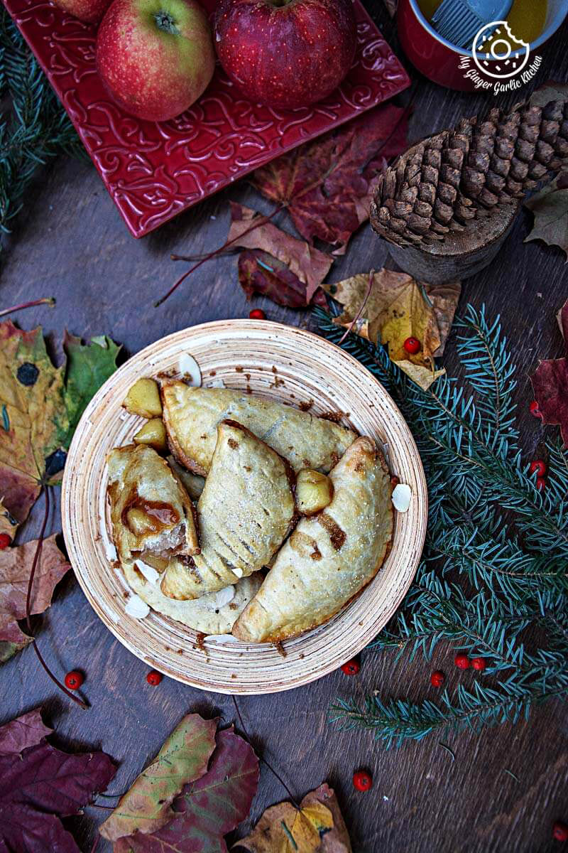 a plate of apple hand pies on a table with apples and pine cones
