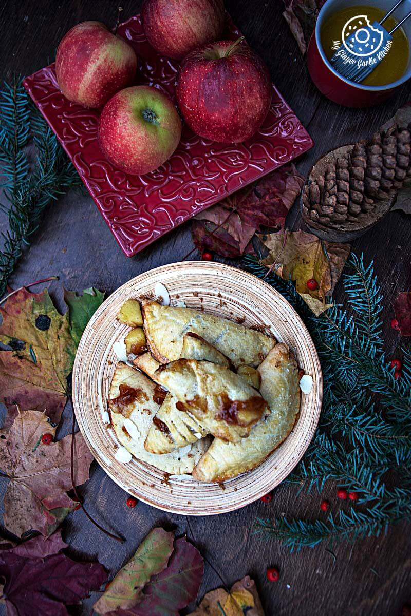 a wooden plate of apple hand pies on a table with apples and leaves
