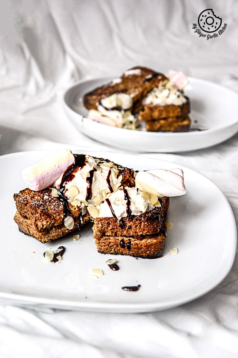two plates of a plate with a banana nutella stuffed cinnamon maple toast whipped cream and chocolate sauce on it on a white table