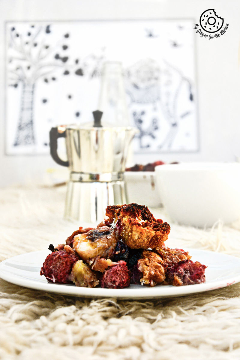 a plate of banana strawberry bread pudding on a table with a silver coffee pot