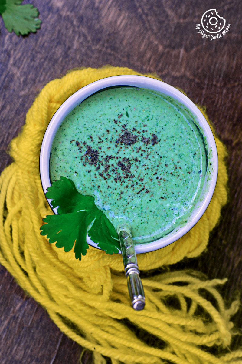 a cup of green tahini dip with a sprig of parsley