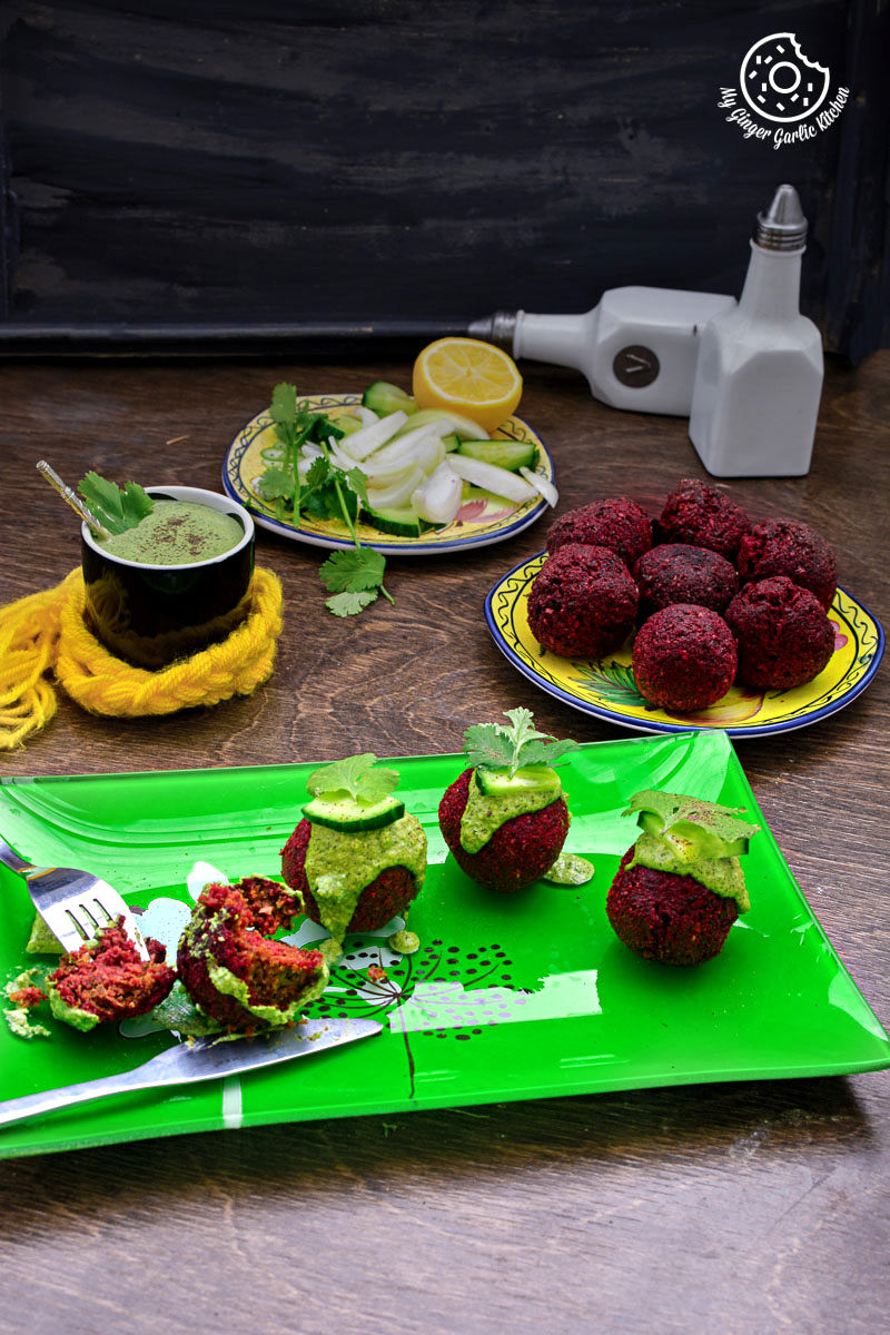 a lot of beet falafels with green tahini dip on the table and some vegetables and falafels in background