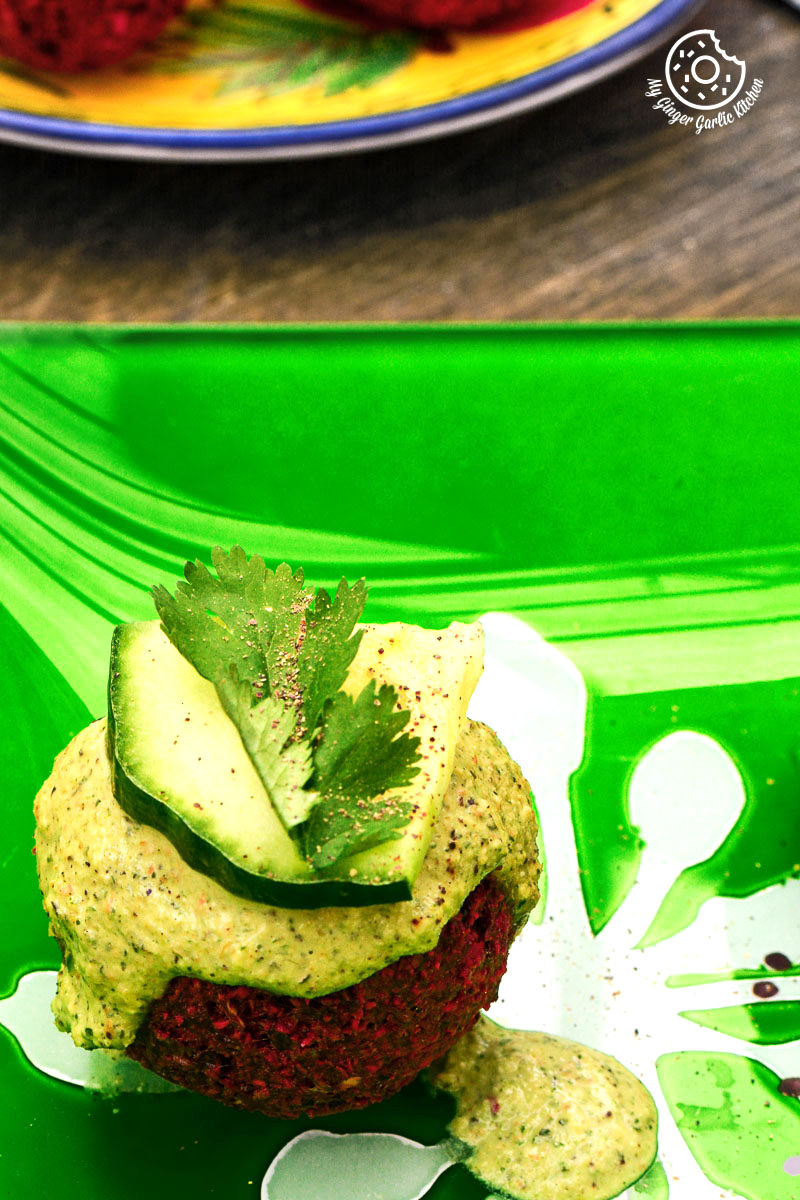 beet falafel with green tahini dip on a green plate with a plate of food