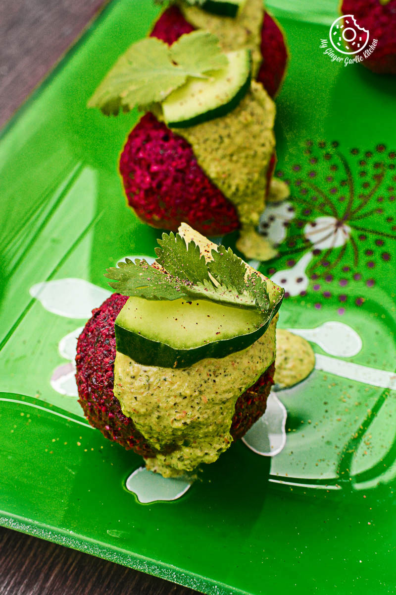 three small beet falafels with green tahini dip on a green plate with a cucumber on top