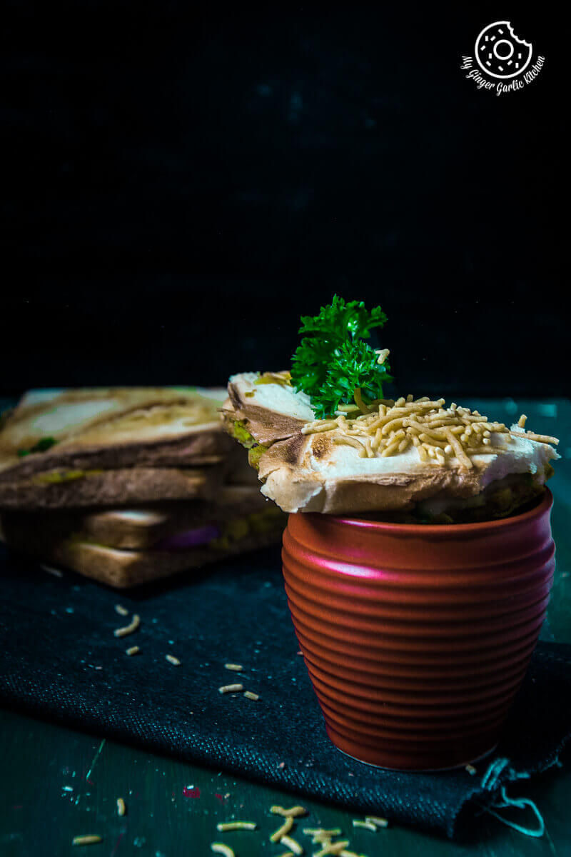a bombay masala toast with sev and a sprig of parsley on top